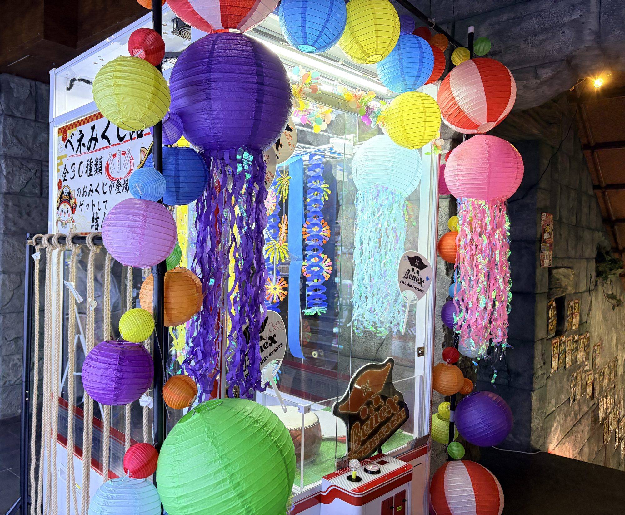 Benex川越店の30周年フォトブース。カラフルなくらげ型ちょうちんの飾り付けと「ベネみくじ 全30種」の掲示、Benex 30th Anniversaryのうちわが並ぶ